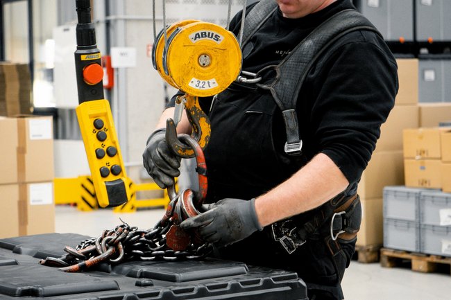 Servicetechniker prüft Lasthaken und Kettengehänge an einem Industriekran